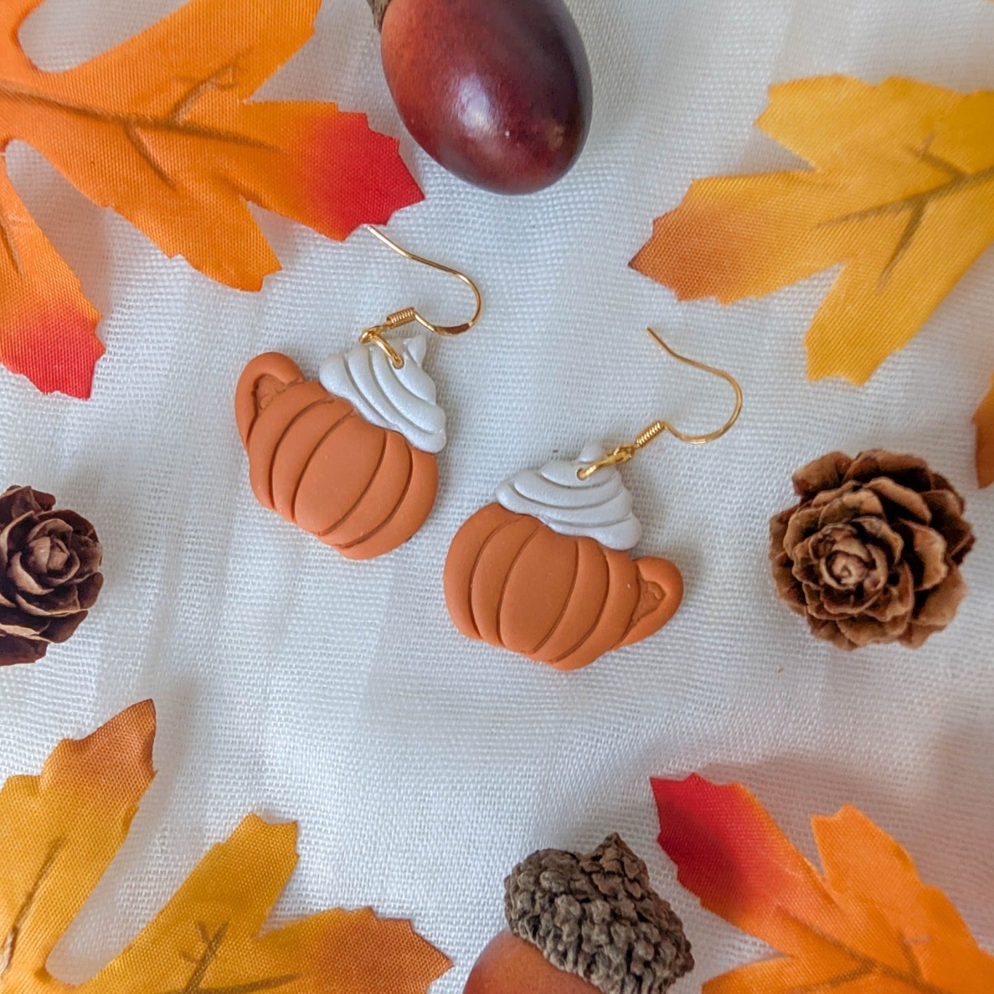 Handmade pumpkin spice latte earrings styled with autumn leaves, pinecones, and acorns