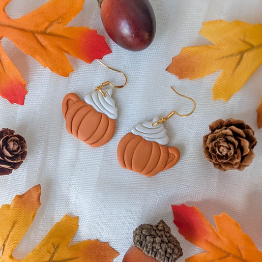Handmade pumpkin spice latte earrings styled with autumn leaves, pinecones, and acorns