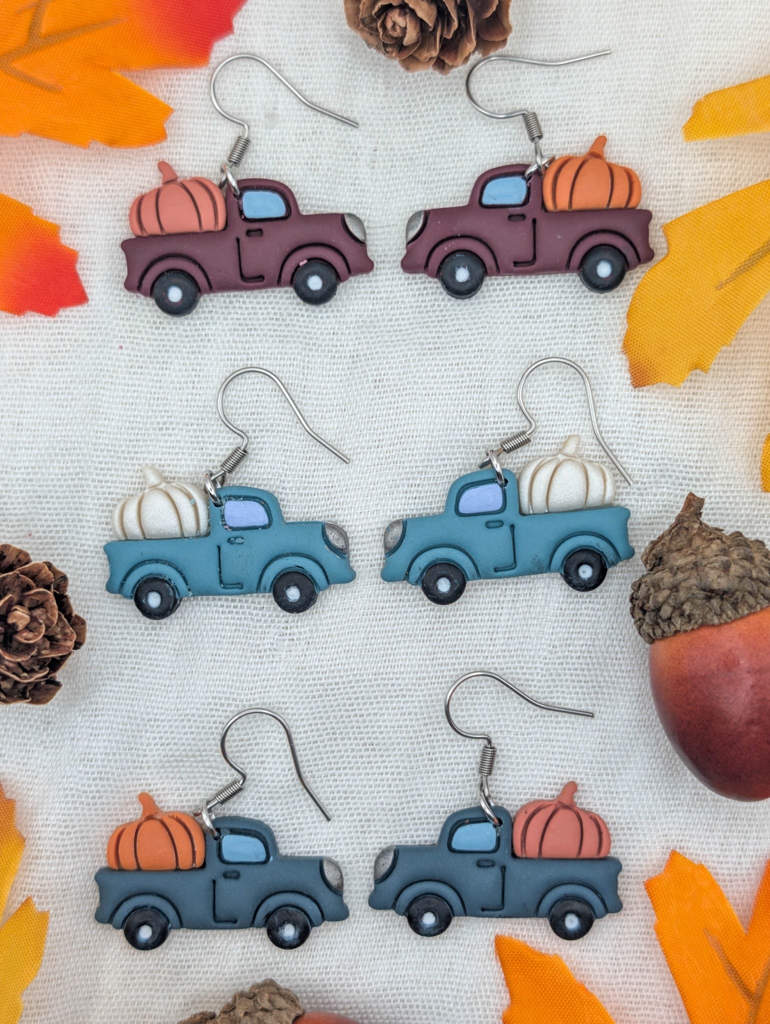 Three color variations of vintage pumpkin truck dangle earrings styled with autumn leaves, pinecones, and acorns