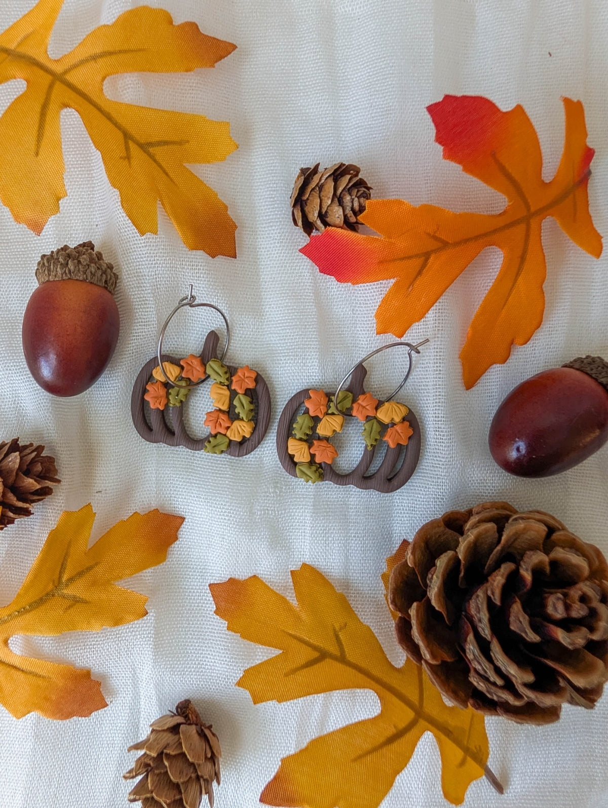 Handmade pumpkin wreath earrings with cascading orange, mustard, and olive fall leaves styled with acorns and pinecones