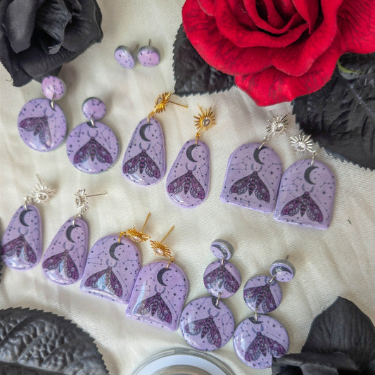 Four styles of purple celestial moth earrings with moon, stars, and gold or silver findings