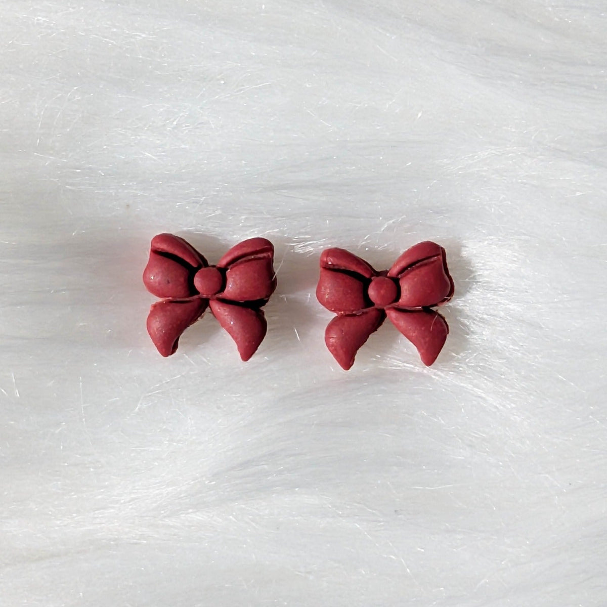 Red polymer clay bow stud earrings on a soft white background