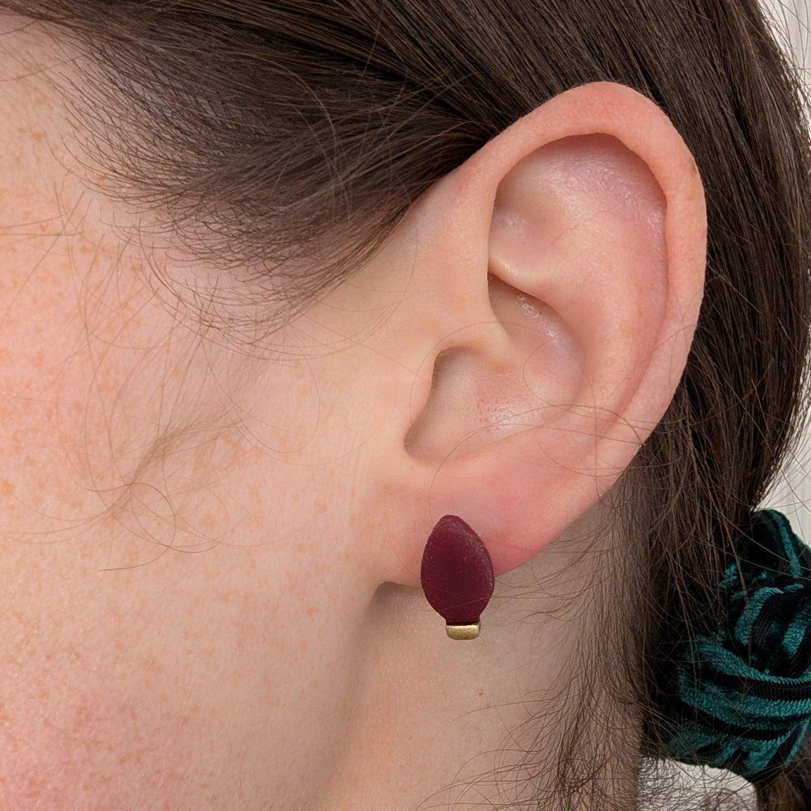 Red and gold Christmas light bulb stud earring shown on ear for scale