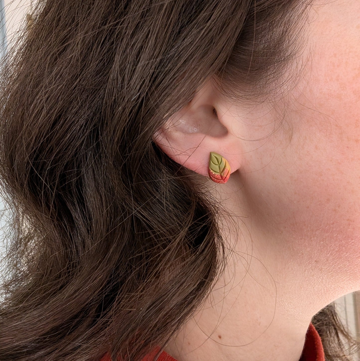 Green autumn leaf stud earring with copper accents worn on ear