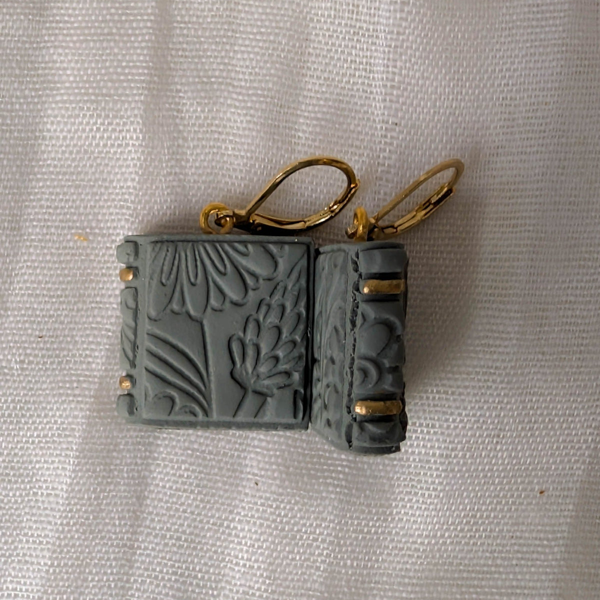 Angled view of embossed Sage Green book earrings with gold binding accents and gold findings