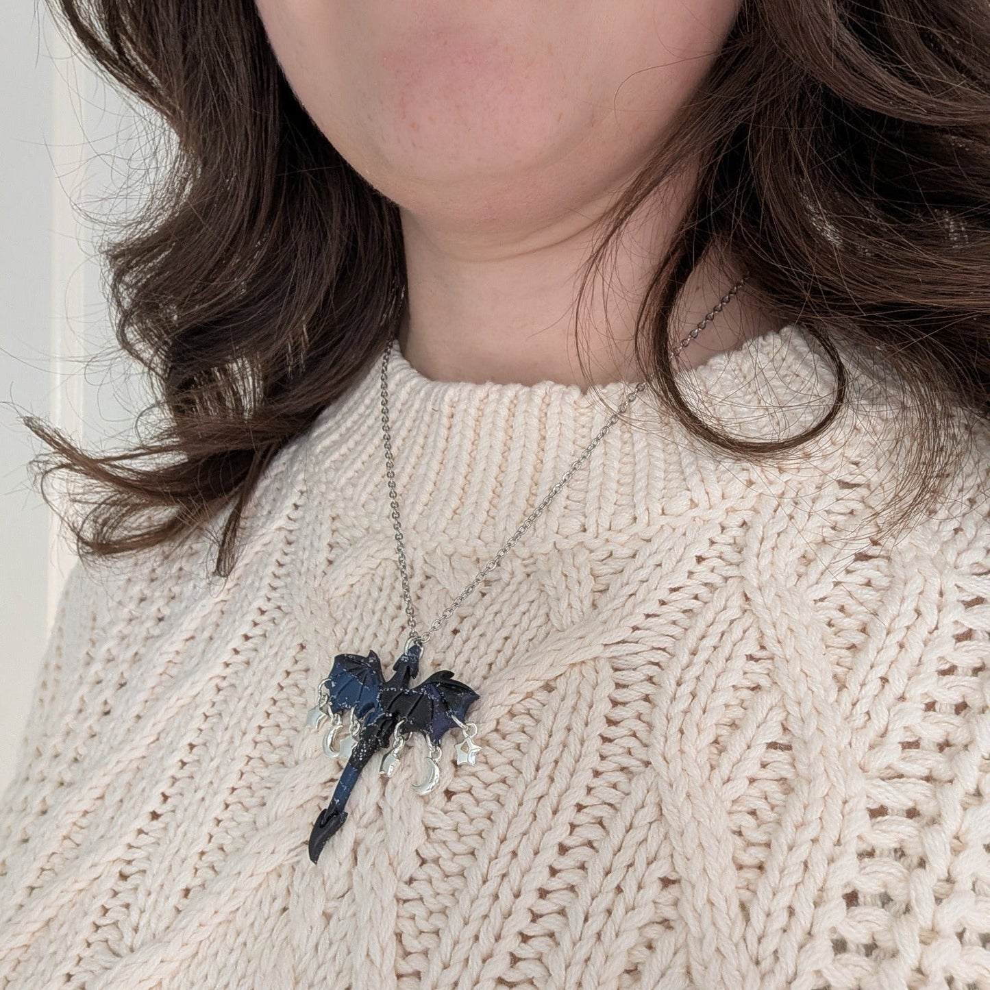 Midnight marble dragon necklace with silver moon and star charms worn over a cream sweater