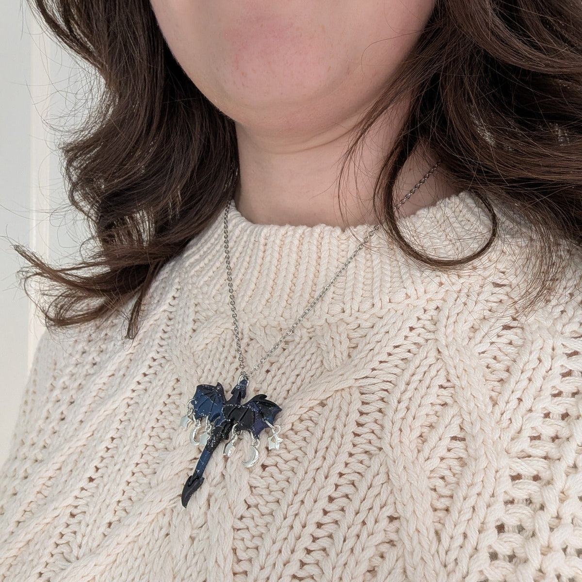 Midnight marble dragon necklace with silver moon and star charms worn over a cream sweater