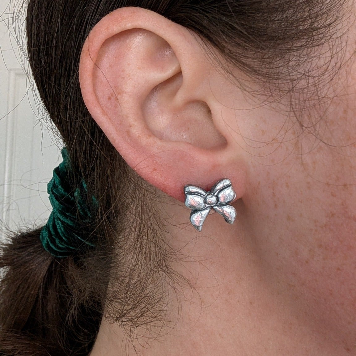Silver foil crackle bow stud earring worn on ear to show its petite 2 cm size