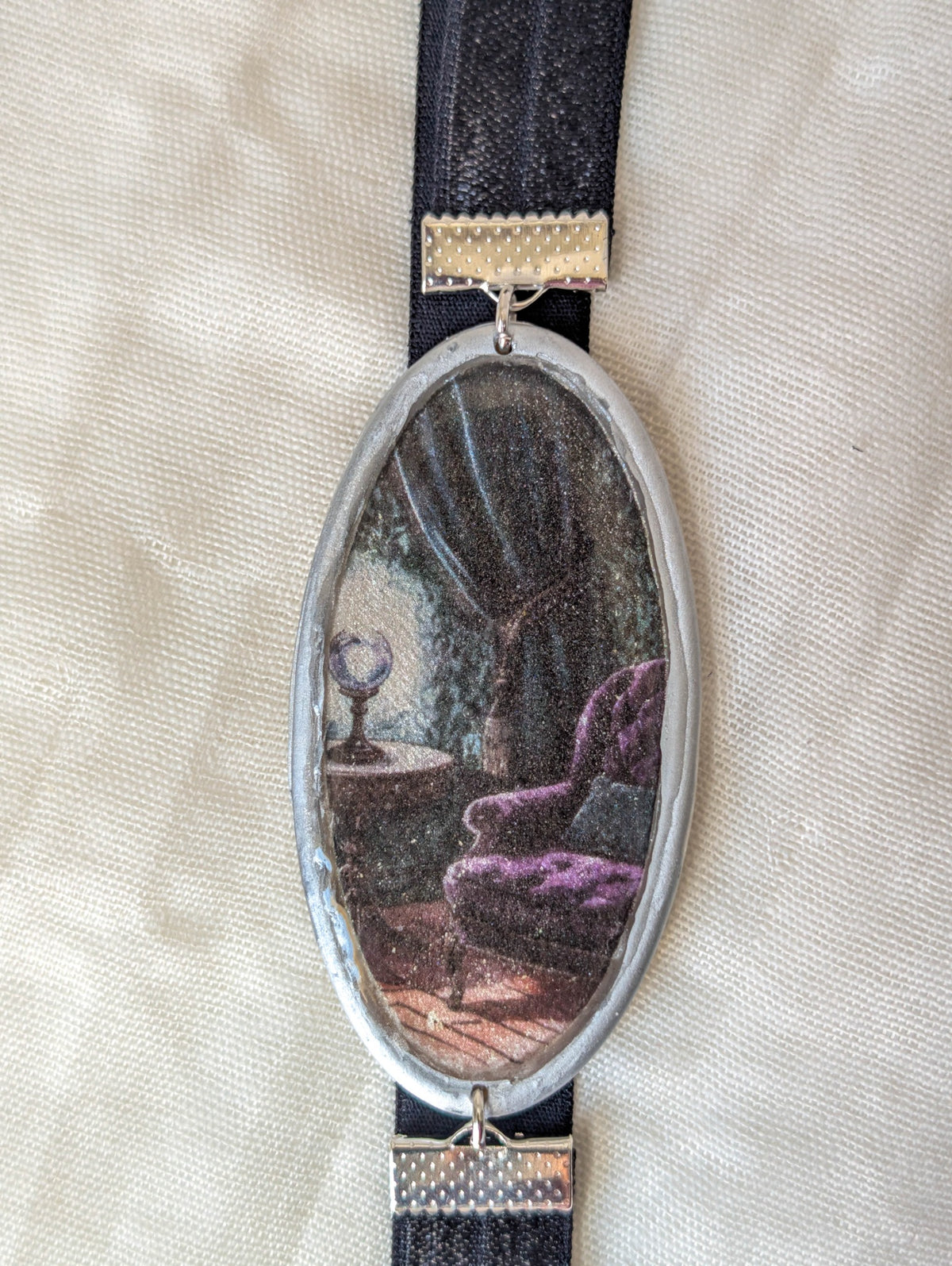 Close-up of silver framed bookmark showing a purple reading chair in a shadowy gothic room