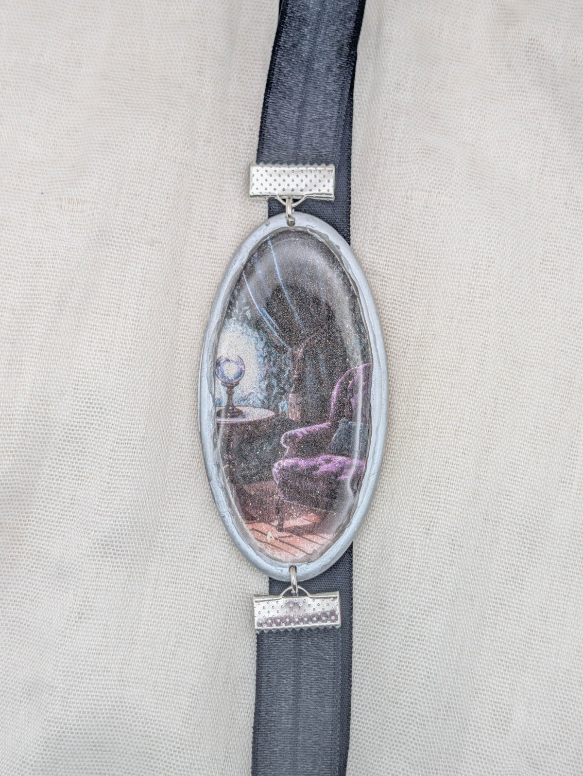 Silver framed gothic polymer clay wrap-around bookmark with a purple reading chair in a shadowy room and black elastic band