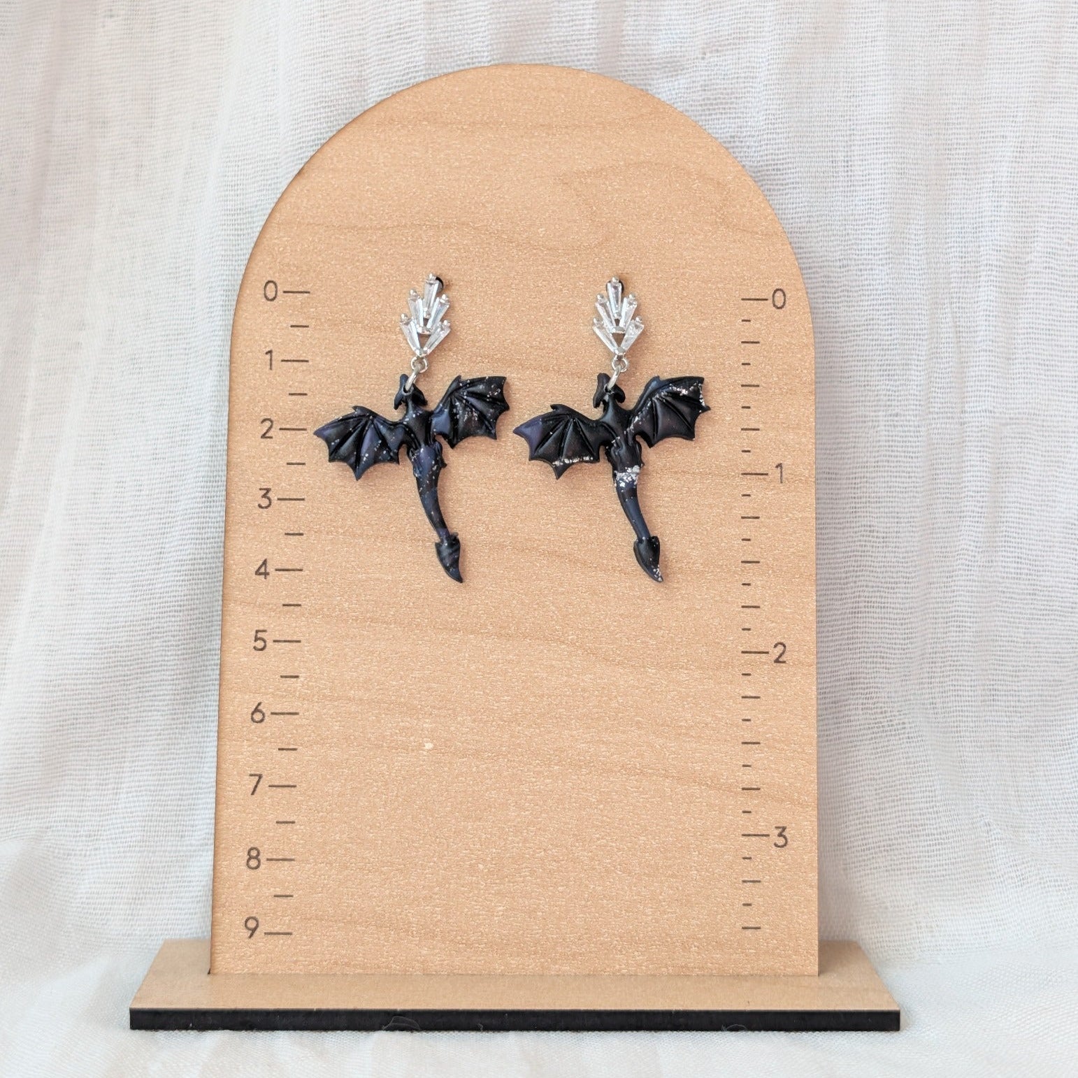 Midnight marble dragon earrings with silver leaf posts displayed beside a ruler