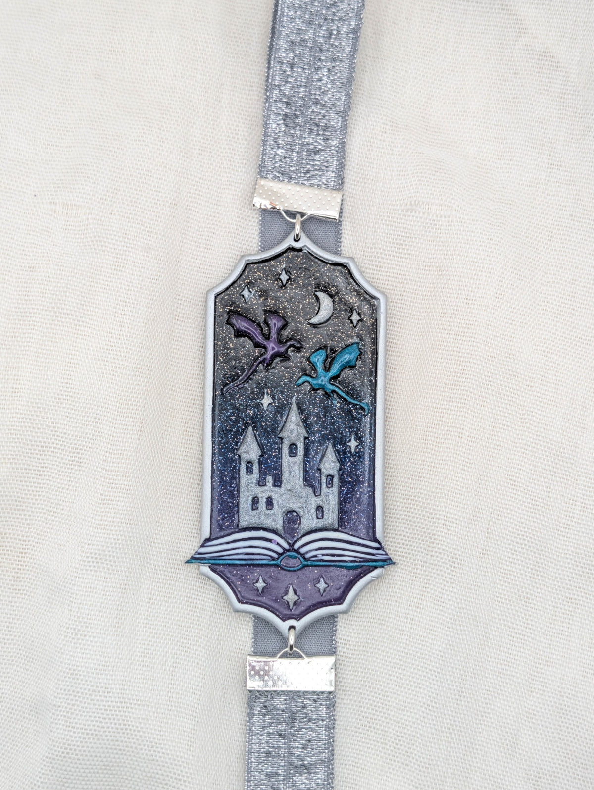Silver framed fantasy polymer clay wrap-around bookmark with purple and blue dragons over a castle and glittering midnight sky