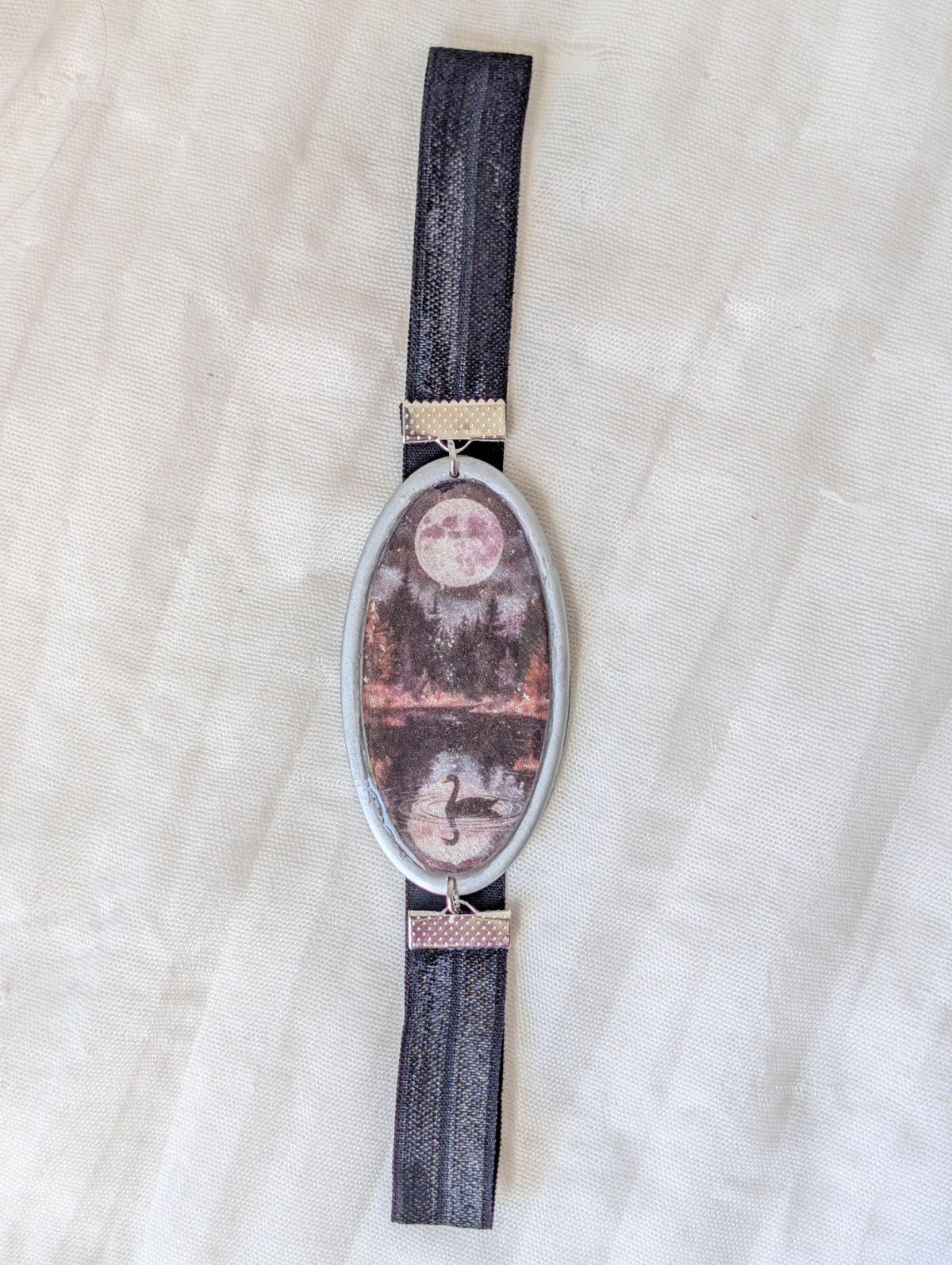 Full view of silver moonlit swan lake polymer clay bookmark with black stretchy band