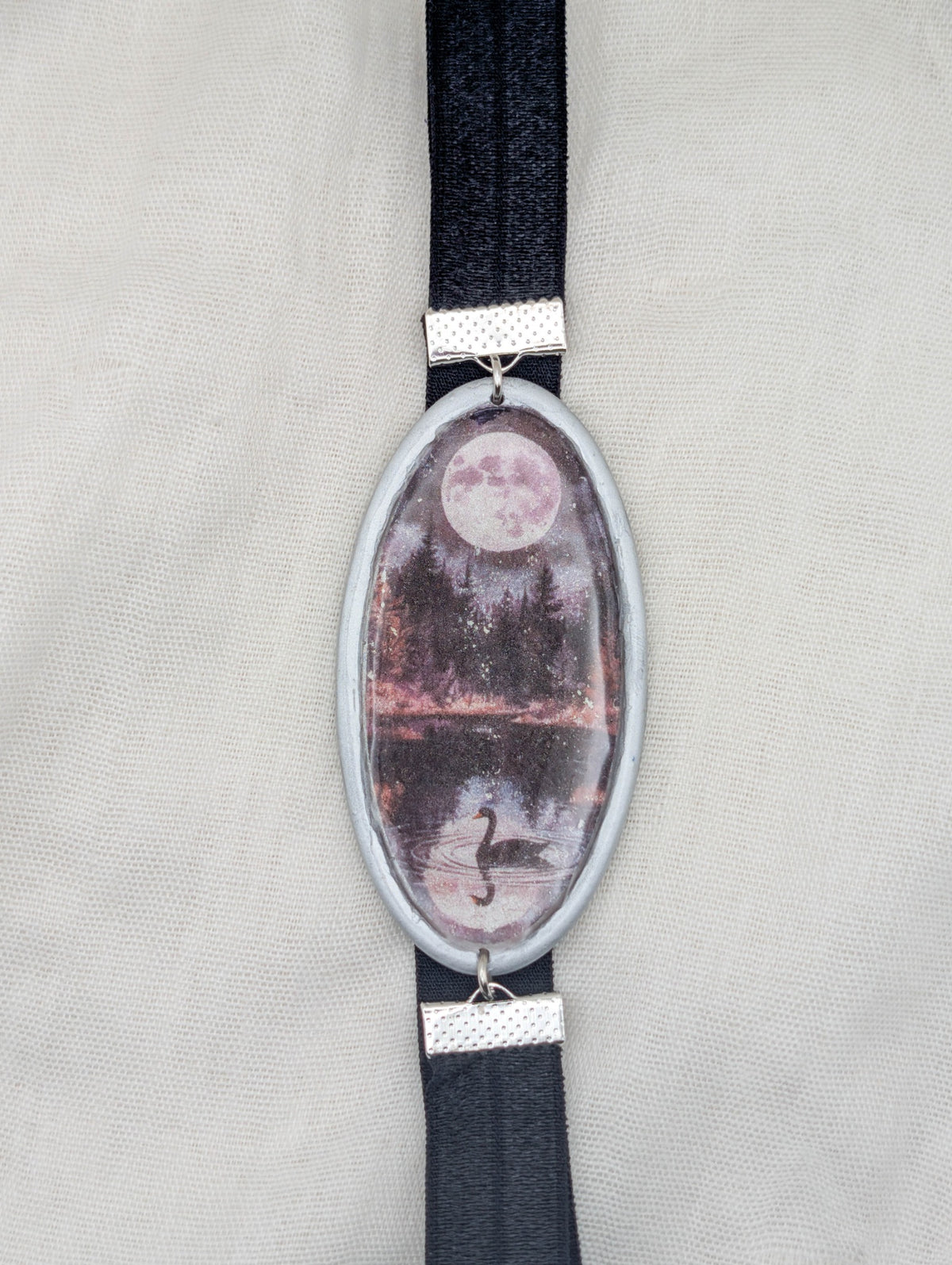 Silver framed gothic polymer clay wrap-around bookmark with a full moon, dark forest, reflective lake, and black swan