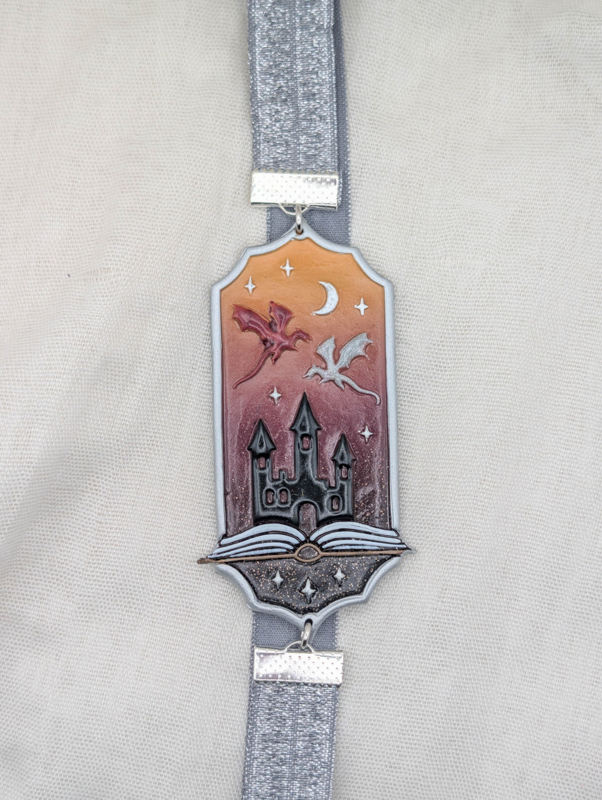 Silver framed fantasy polymer clay wrap-around bookmark with dragons, castle, crescent moon, and rose pink background