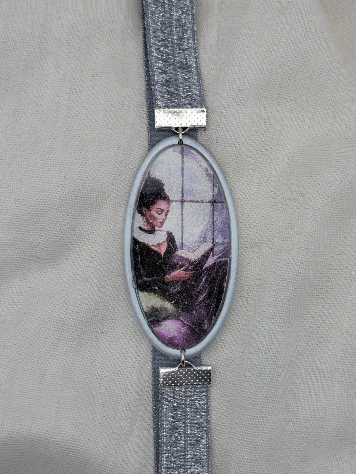 Silver framed polymer clay wrap-around bookmark showing a woman reading by a window with silver elastic band