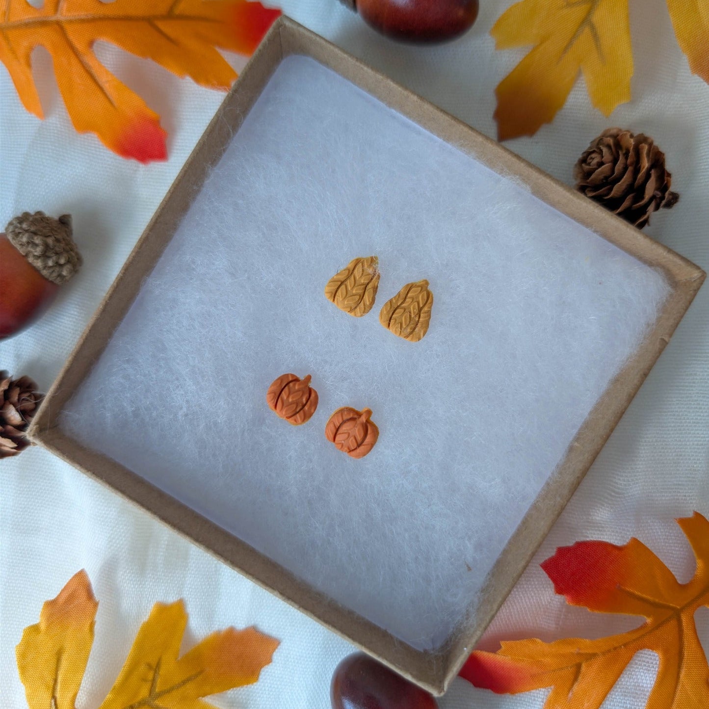 Tiny burnt orange pumpkin and mustard yellow gourd stud earrings with knitted texture in an autumn display
