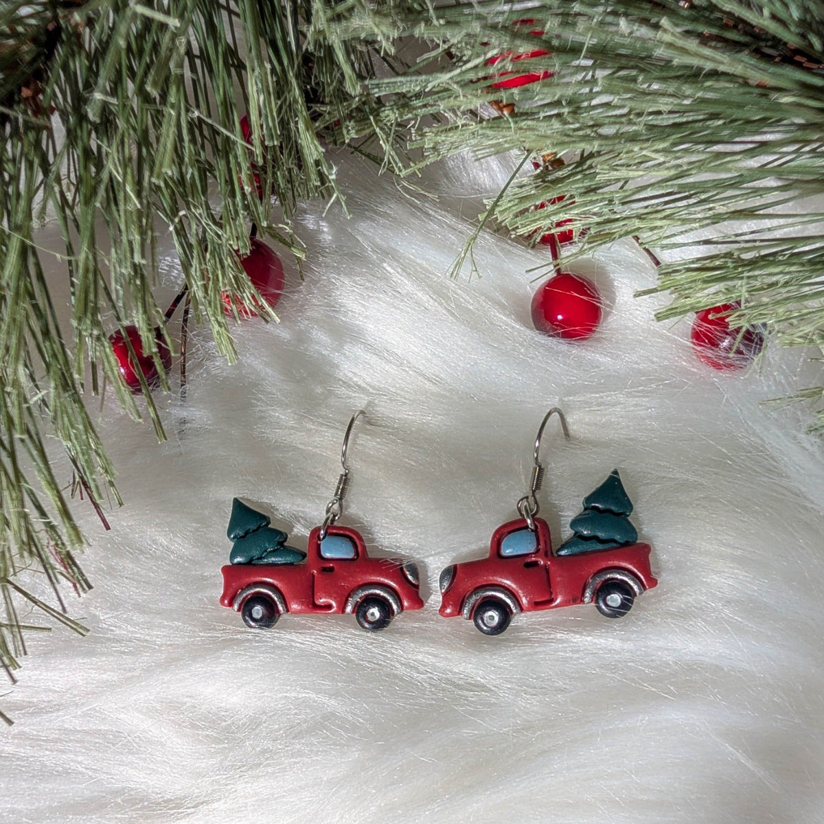 Pair of red Christmas tree truck earrings styled with festive evergreen branches