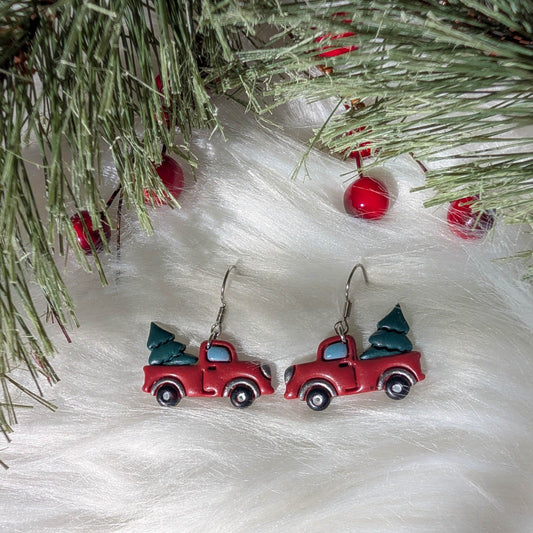 Pair of red Christmas tree truck earrings styled with festive evergreen branches